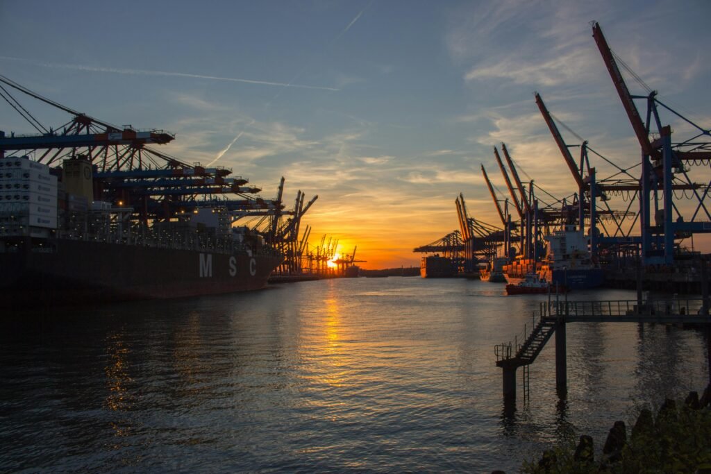 Shipping vessels at Hamburg port during a vibrant sunset, showcasing industrial cranes.